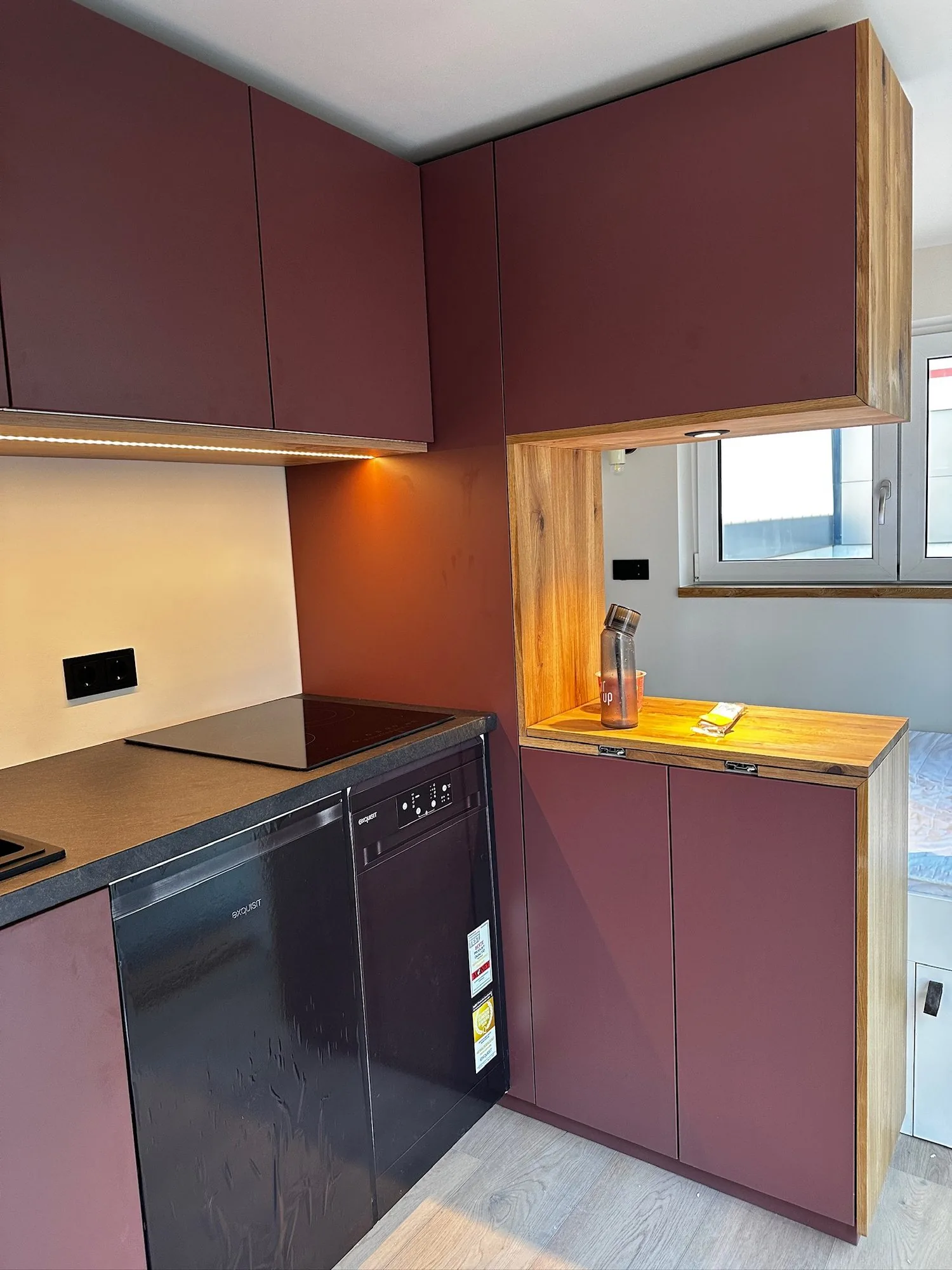 Tiny House 15 m² von Contain-us – Küchenzeile in Dunkelrot mit Kochfeld, Hängeschränken und Fenster