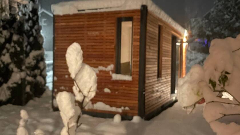 Beleuchtetes Tiny House im Schnee, Lichtschein aus Fenster und Schiebefront