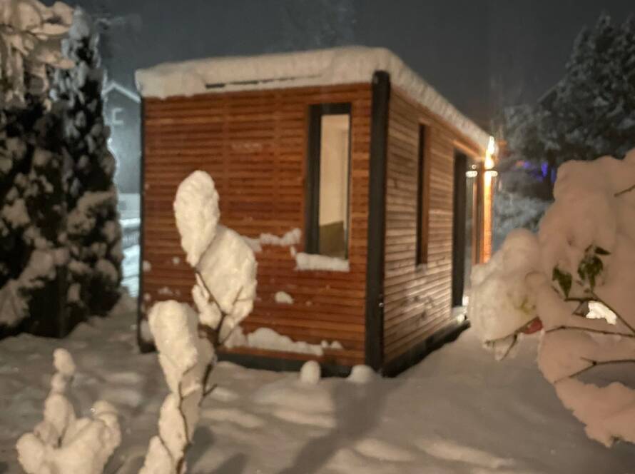 Beleuchtetes Tiny House im Schnee, Lichtschein aus Fenster und Schiebefront