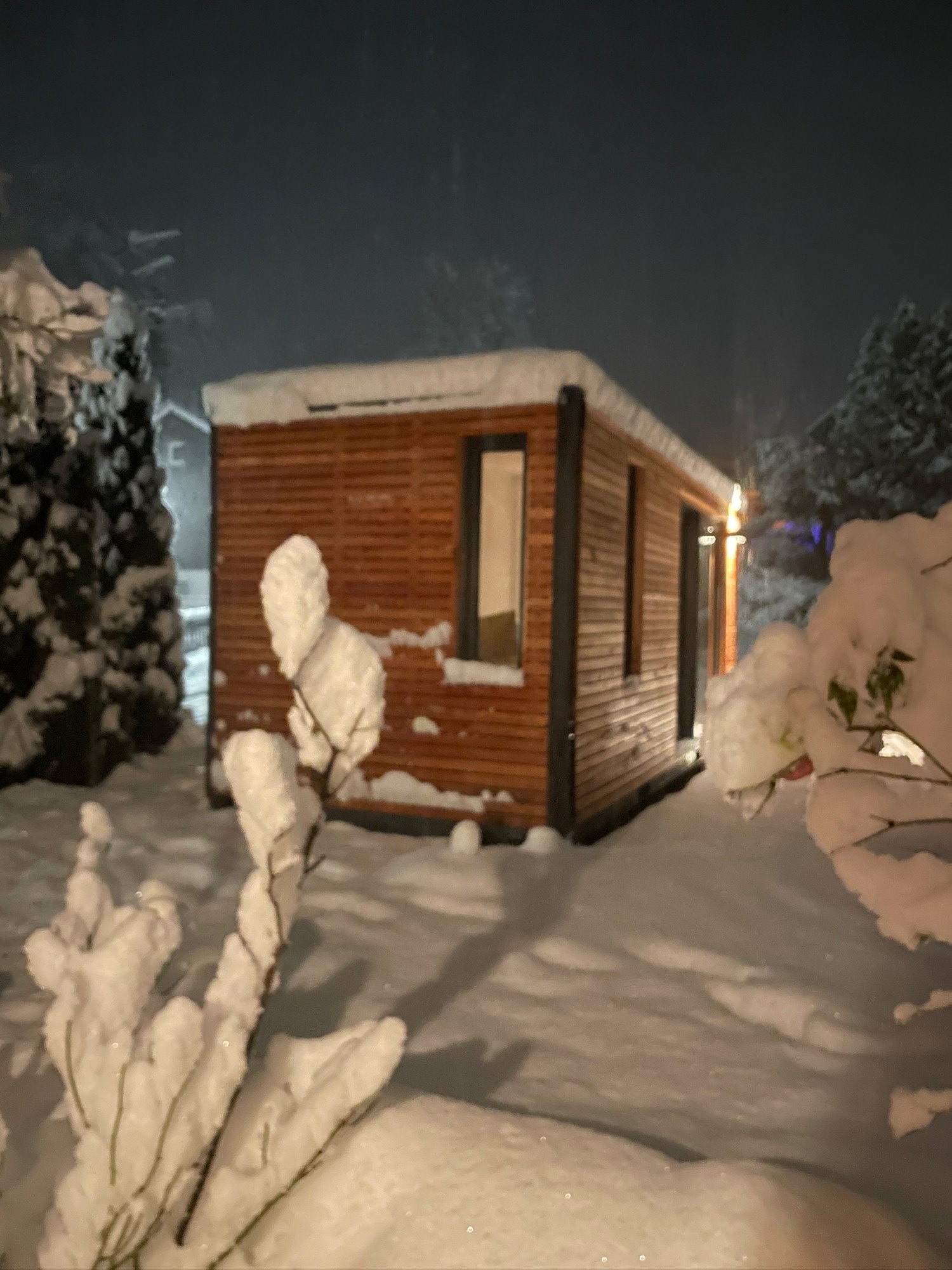 Beleuchtetes Tiny House im Schnee, Lichtschein aus Fenster und Schiebefront