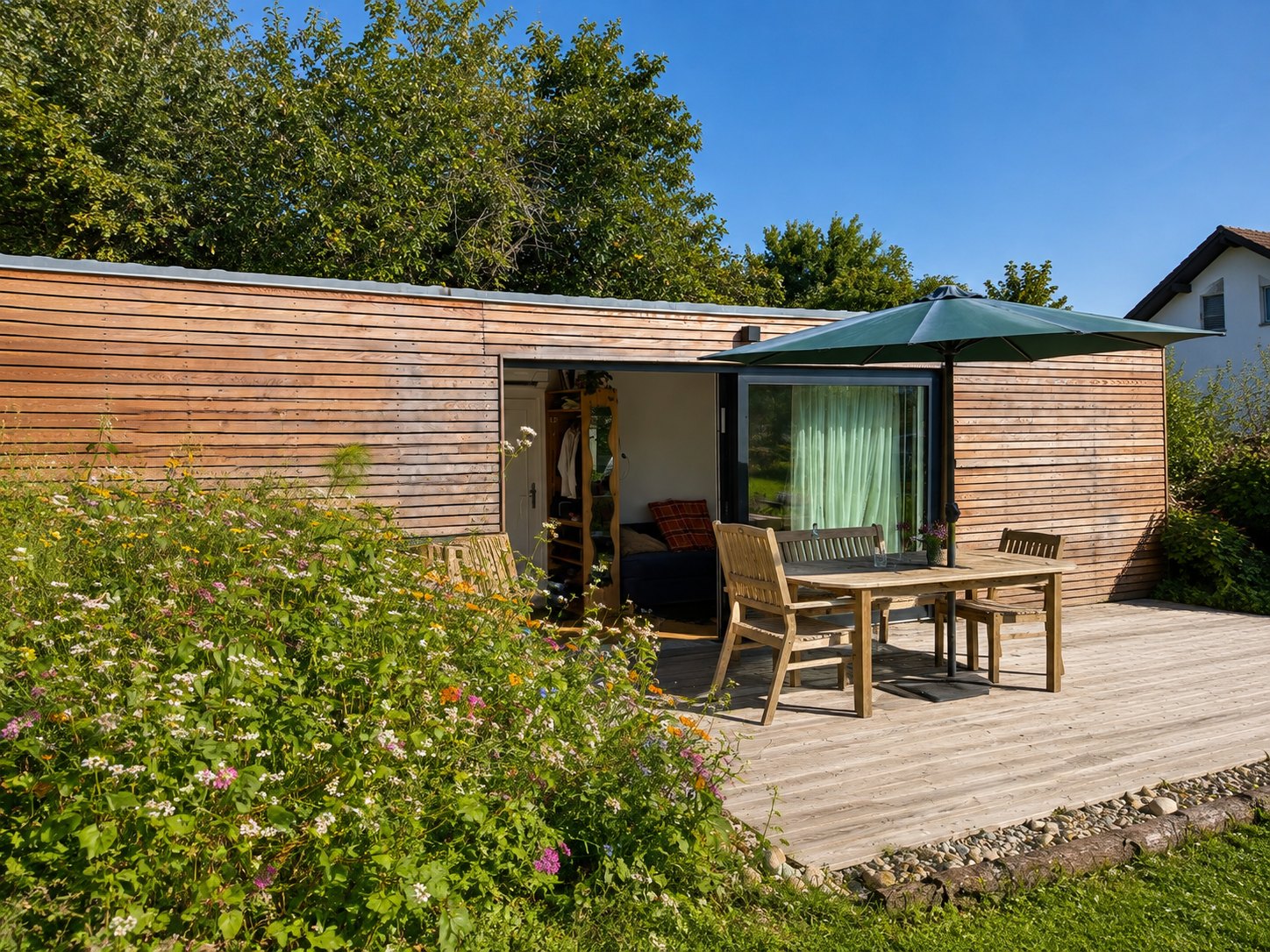 Tiny House 30 m² von Contain-us – Blick über das Blumenbeet auf die Terrasse mit Sitzgruppe