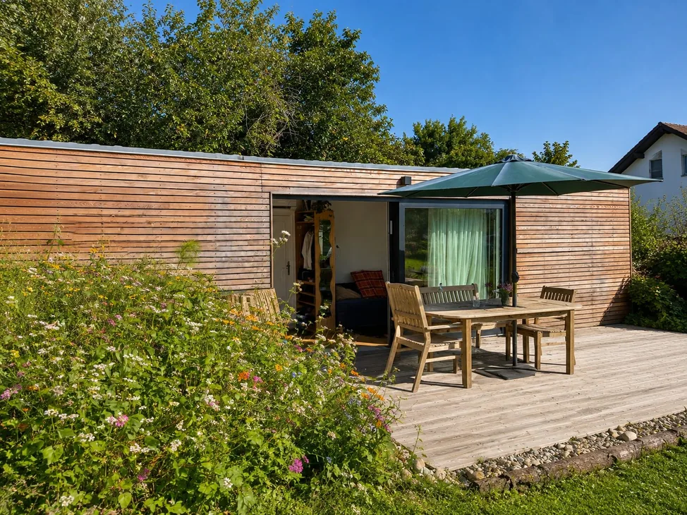 Tiny House 30 m² von Contain-us – Blick über das Blumenbeet auf die Terrasse mit Sitzgruppe