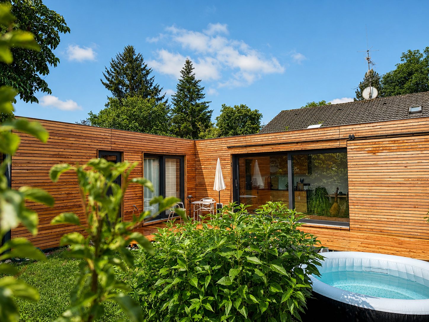 Tiny House 45 m² von Contain-us – Blick durch Sträucher auf die Holzfassade, im Vordergrund ein Aufstellpool