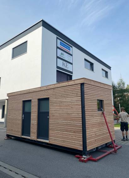 Gartenhaus 15 m² von Contain-us – das Modul steht auf Rangierrollen vor einem Wohnhaus und wird an seinen Platz geschoben