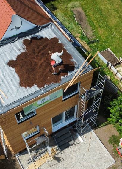 Hausanbau 60 m² von Contain-us – die Dachbegrünung wird auf dem Anbau aufgebracht, daneben das Ziegeldach des Bestandshauses
