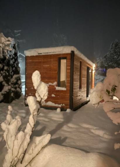 Beleuchtetes Tiny House im Schnee, Lichtschein aus Fenster und Schiebefront