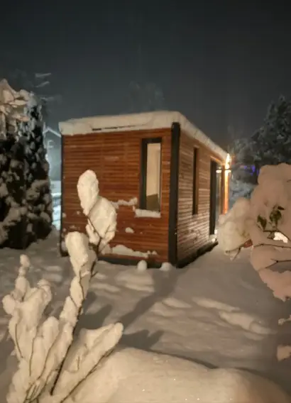 Beleuchtetes Tiny House im Schnee, Lichtschein aus Fenster und Schiebefront